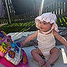 Lilah is registered to the contest to win money with this photo: baby, child, pink_hat, white_outfit, toy, colorful_toy, play_mat, outdoor, sunlight, sunbeam, grass, fence, playtime, smiling, sitting, cute, happy, summer, infant, fun