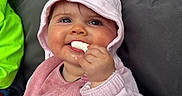 Lilah joined the competition — help win amazing prizes! baby, child, pink_hoodie, bib, snack, smile, face, happy, cushion, gray_background, hand, cheeks, eyes, indoors, cozy, clothing, person, cute, infant, munching