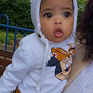 Seyana a rejoint le concours — aidez-le/la à gagner de superbes lots ! baby, child, white_hat, mickey_mouse, sweatshirt, orange_pants, floral_pattern, person, hand, outdoor, bench, greenery, railing, curly_hair, expression, portrait, cute, holding, nature, clothing