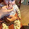 Cléo a rejoint le concours — aidez-le/la à gagner de superbes lots ! adult_hand, baby, blue_eyes, child, closeup, cozy, curious, family, furniture, giraffe_pattern, hand, holding, indoor, infant, nibbling, onesie, person, seated, warm_lighting, wooden_floor