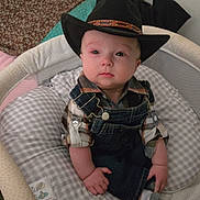 Isaiah joined the competition — help win amazing prizes! baby, child, cowboy_hat, portrait, sitting, infant, serious_expression, wide_eyes, denim_overalls, plaid_shirt, crib, baby_seat, cushion, blanket, bedroom, indoors, patterned_fabric, cowboy_costume, cute, photography