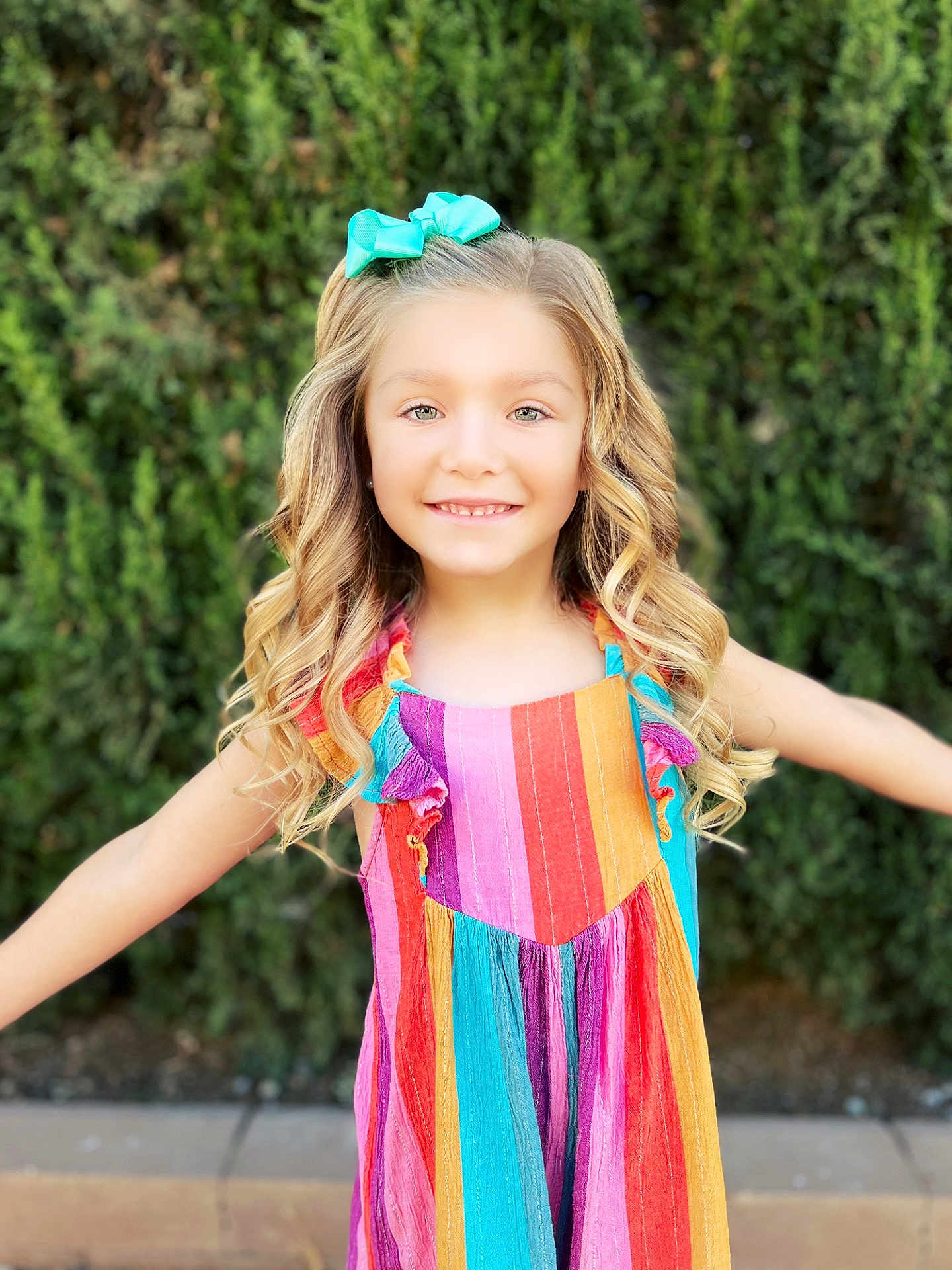 Velouria joined the competition — help win amazing prizes! child, girl, smiling, curly_hair, blonde, bow, colorful_dress, striped_dress, outdoor, greenery, hedge, happy, portrait, sunny, arms_outstretched, fashion, person, cute, youth, nature