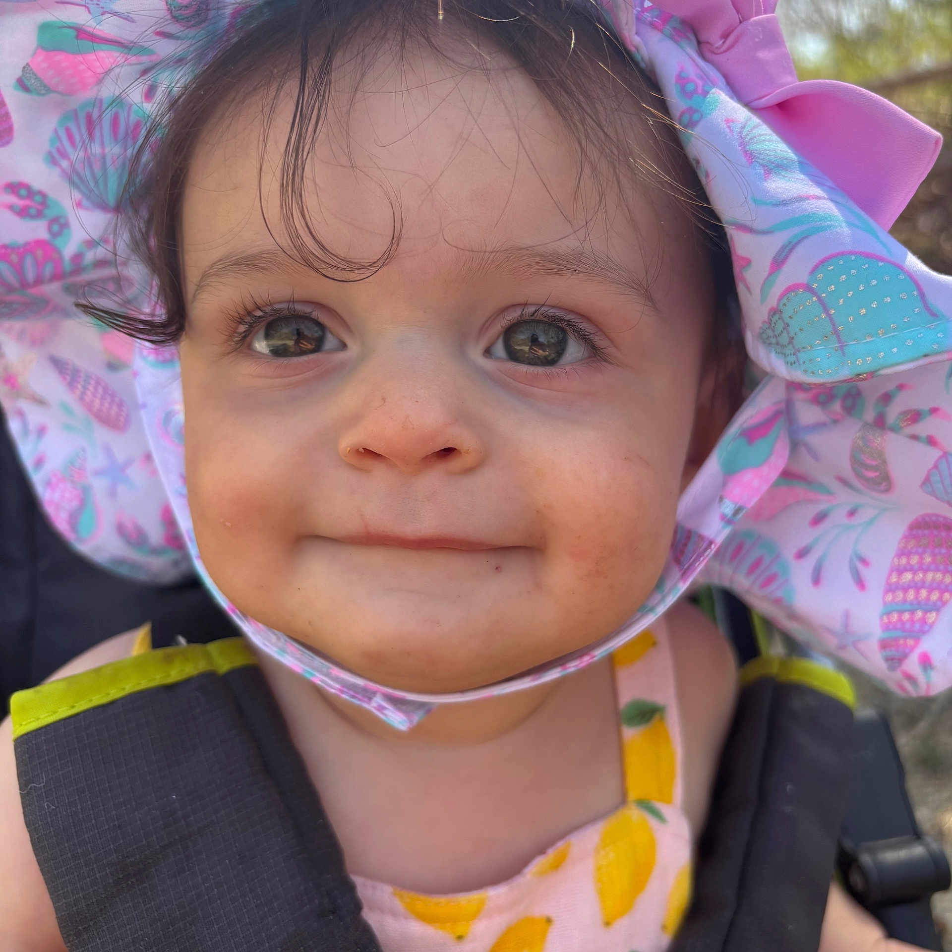 Jade is registered to the contest to win money with this photo: toddler, child, face, smile, hat, sunhat, outdoor, baby, curly_hair, closeup, summer_clothing, yellow, pink, blue, patterned_clothing, cute, portrait, daylight, expression, young_child