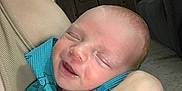 Wesley is registered to the contest to win money with this photo: baby, sleeping, infant, blue_clothing, adult_arm, indoor, living_room, television, couch, carpet, wooden_furniture, holding, cozy, relaxed, peaceful, closeup, person, face, skin, hand