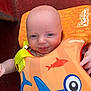 baby, child, face, smile, blue_eyes, floatation_vest, orange, blue, fish_pattern, shark_design, red_background, infant, cute, clothing, closeup, portrait, happy, baby_girl_or_boy, baby_accessory, indoor