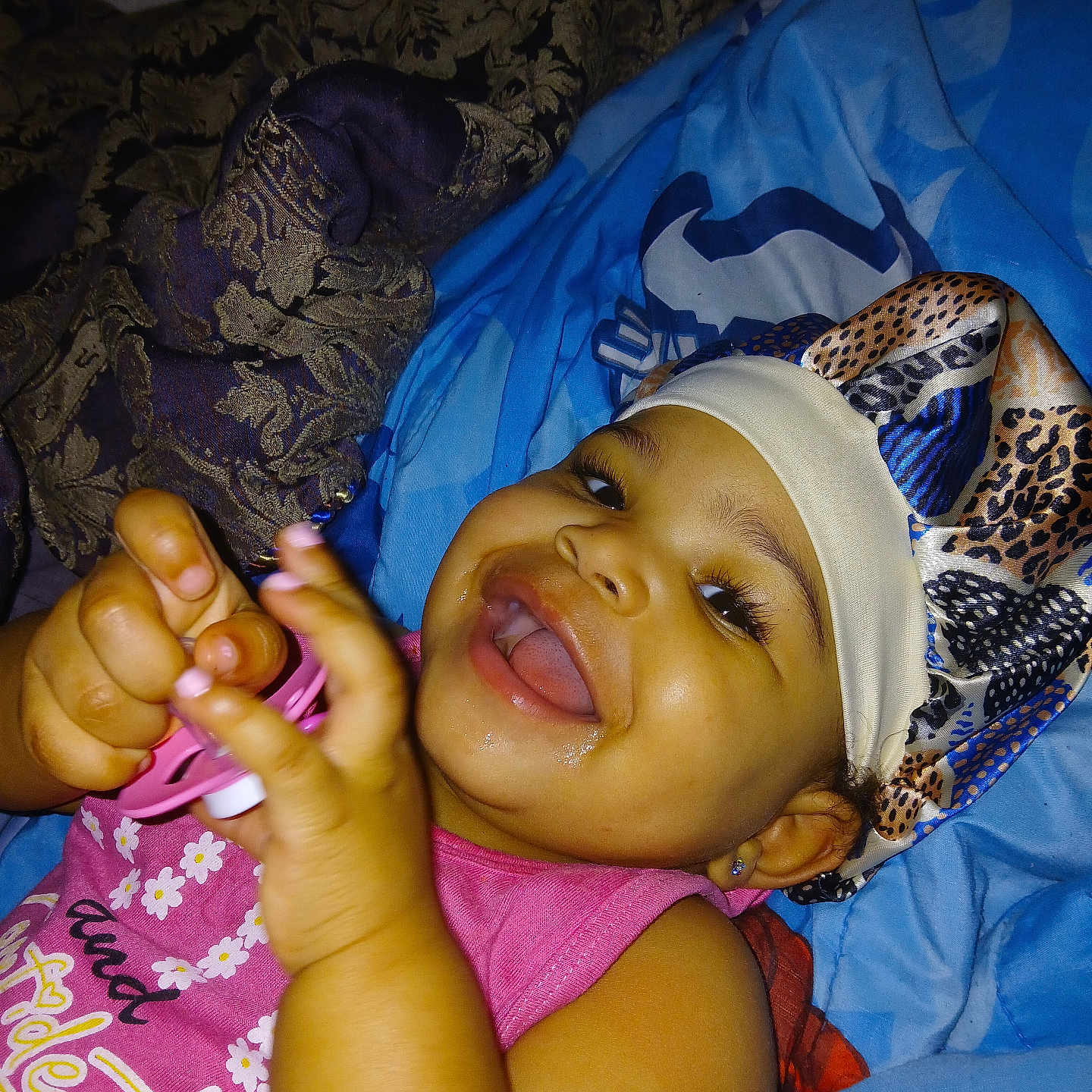 Na'Kiah joined the competition — help win amazing prizes! baby, blue_blanket, bonnet, child, cute, expression, fabric, face, fingernails, hand, happy, headwear, indoor, lying_down, pacifier, person, pink_shirt, portrait, skin, smiling