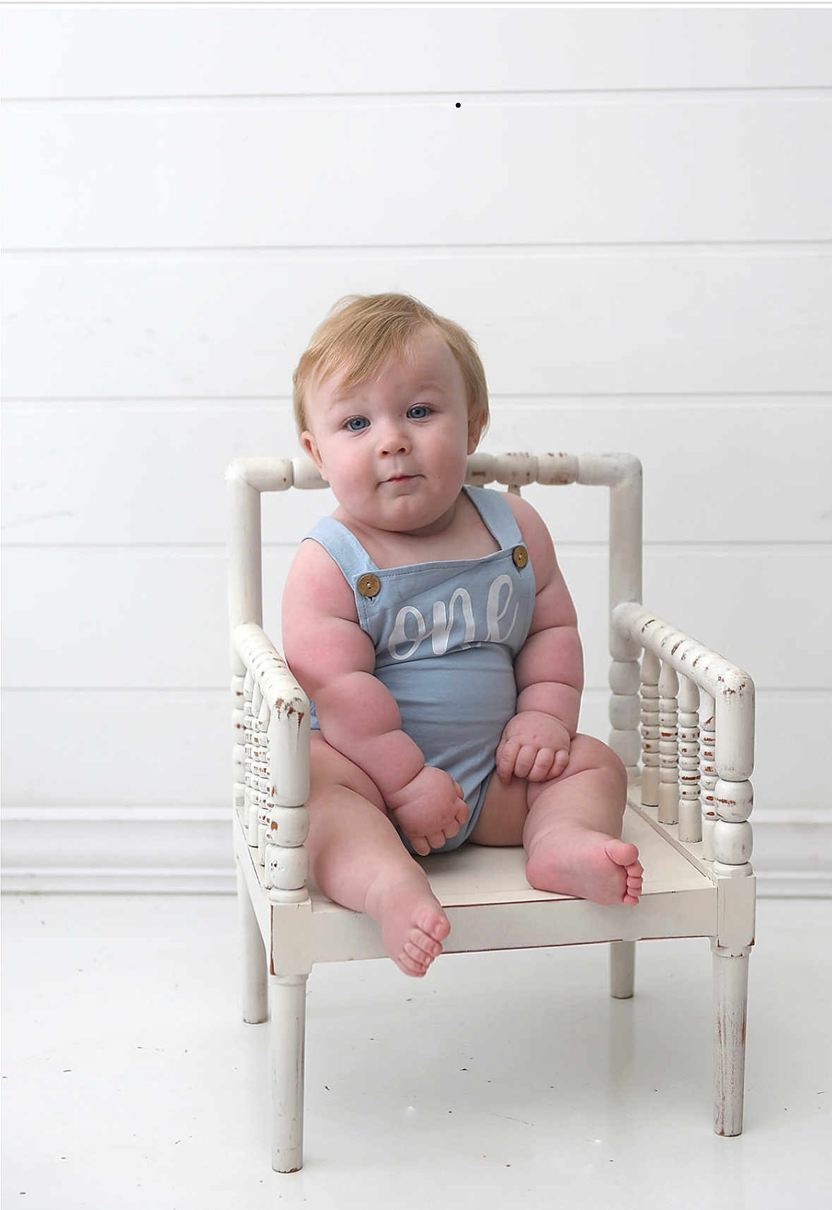 Rhett joined the competition — help win amazing prizes! baby, child, infant, blue_romper, white_chair, wooden_chair, sitting, portrait, cute, chubby, plump, indoor, minimalistic, white_background, expression, curious, hands, feet, blonde_hair, face