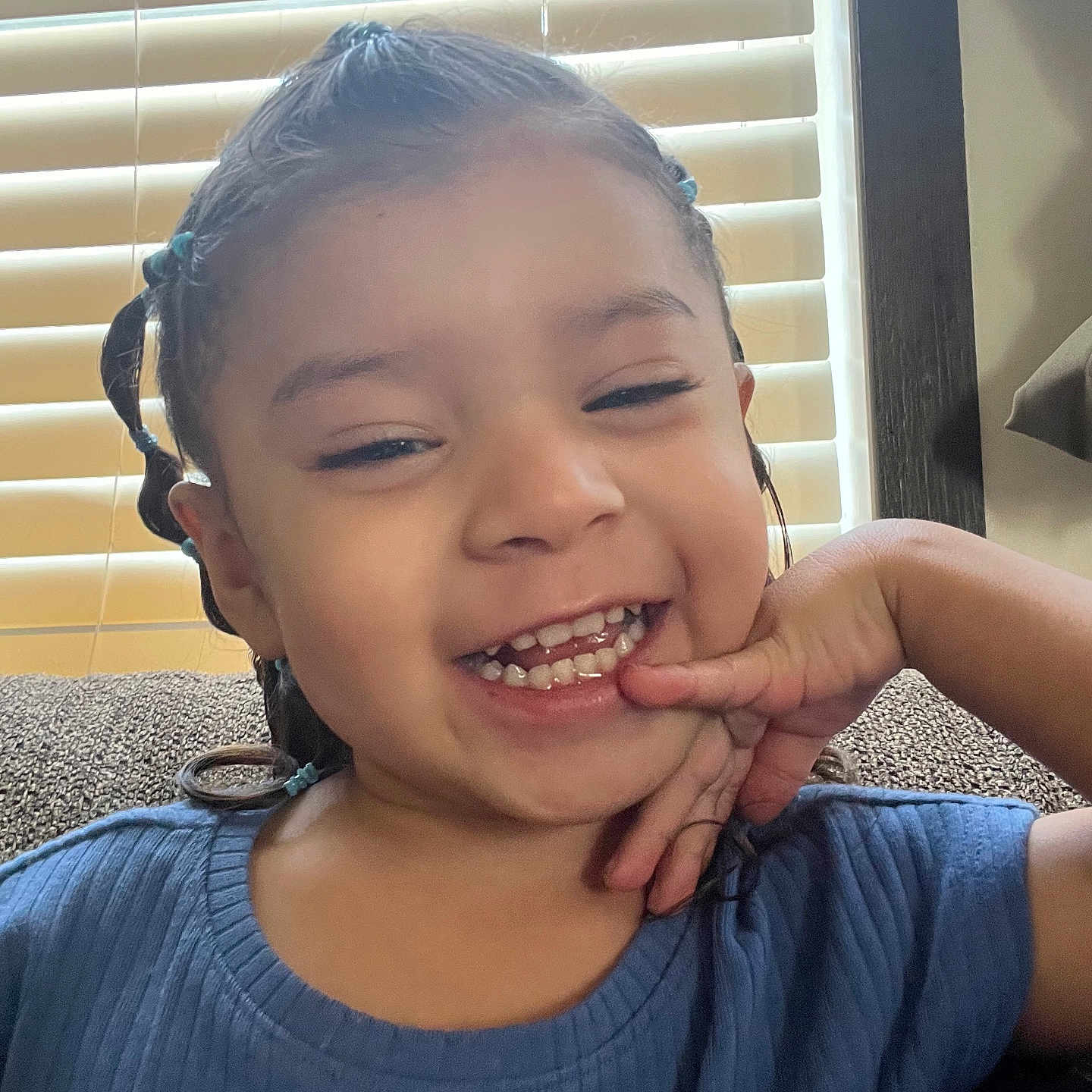 Alaïa joined the competition — help win amazing prizes! blinds, blue_shirt, braids, casual, child, couch, cute, face, hair, hand, happy, indoor, light, person, portrait, relaxed, smiling, teeth, toddler, window
