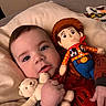 baby, child, teddy_bear, stuffed_toy, woody_doll, pillow, indoor, bed, cute, portrait, infant, soft_lighting, red_clothing, hand, face, eyes, toy_story, plush, smile, cozy