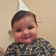 Younes is registered to the contest to win money with this photo: baby, child, smiling, paper_hat, batman_shirt, indoor, person, cute, portrait, face, cheeks, happy, young_child, hand, clothing, dark_hair, seated, wallpaper, infant, playful
