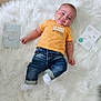 baby, infant, child, smile, orange_shirt, jeans, white_rug, wooden_floor, milestone_cards, lying_down, cute, fluffy, flooring, casual_clothing, indoor, happy, portrait, cheeky, young_child, bright_colors