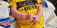 Dallas is registered to the contest to win money with this photo: baby, smiling, yellow_tshirt, awesome_brother, camo_pants, towel, medical_tape, indoor, lying_down, child, cute, happy, infant, face, person, skin, clothing, fabric, baby_boy, casual