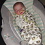baby, sleeping, swaddle, monkey_pattern, baby_seat, nasal_tube, infant, soft_toy, cozy, child, cute, resting, medical, comfort, indoors, blanket, wearing, patterned_clothing, peaceful, young_child