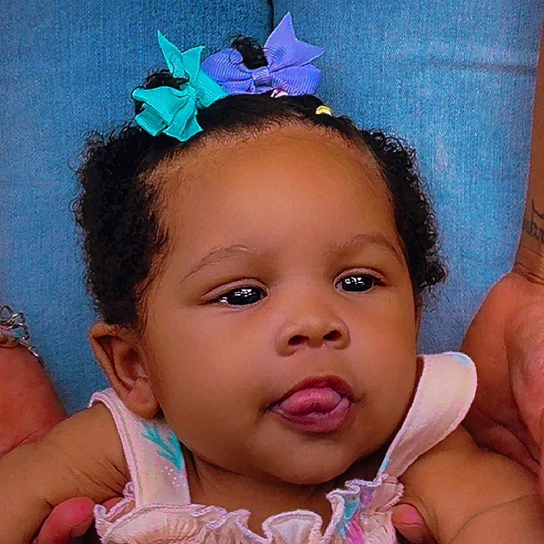 Kazelyn joined the competition — help win amazing prizes! baby, blue_background, child, closeup, curly_hair, cute, expression, face, hair_bow, head, holding_hands, infant, person, pink_clothing, playful, portrait, skin, smiling, tongue, young