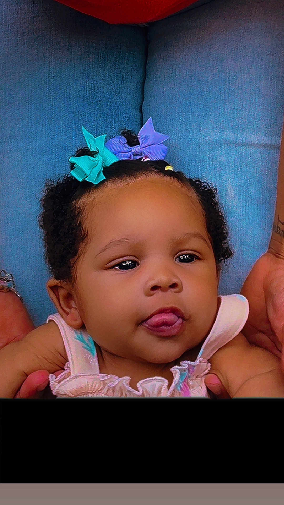 Kazelyn joined the competition — help win amazing prizes! baby, child, face, tongue, hair_bow, curly_hair, smiling, person, holding_hands, blue_background, cute, infant, portrait, pink_clothing, playful, skin, head, expression, closeup, young