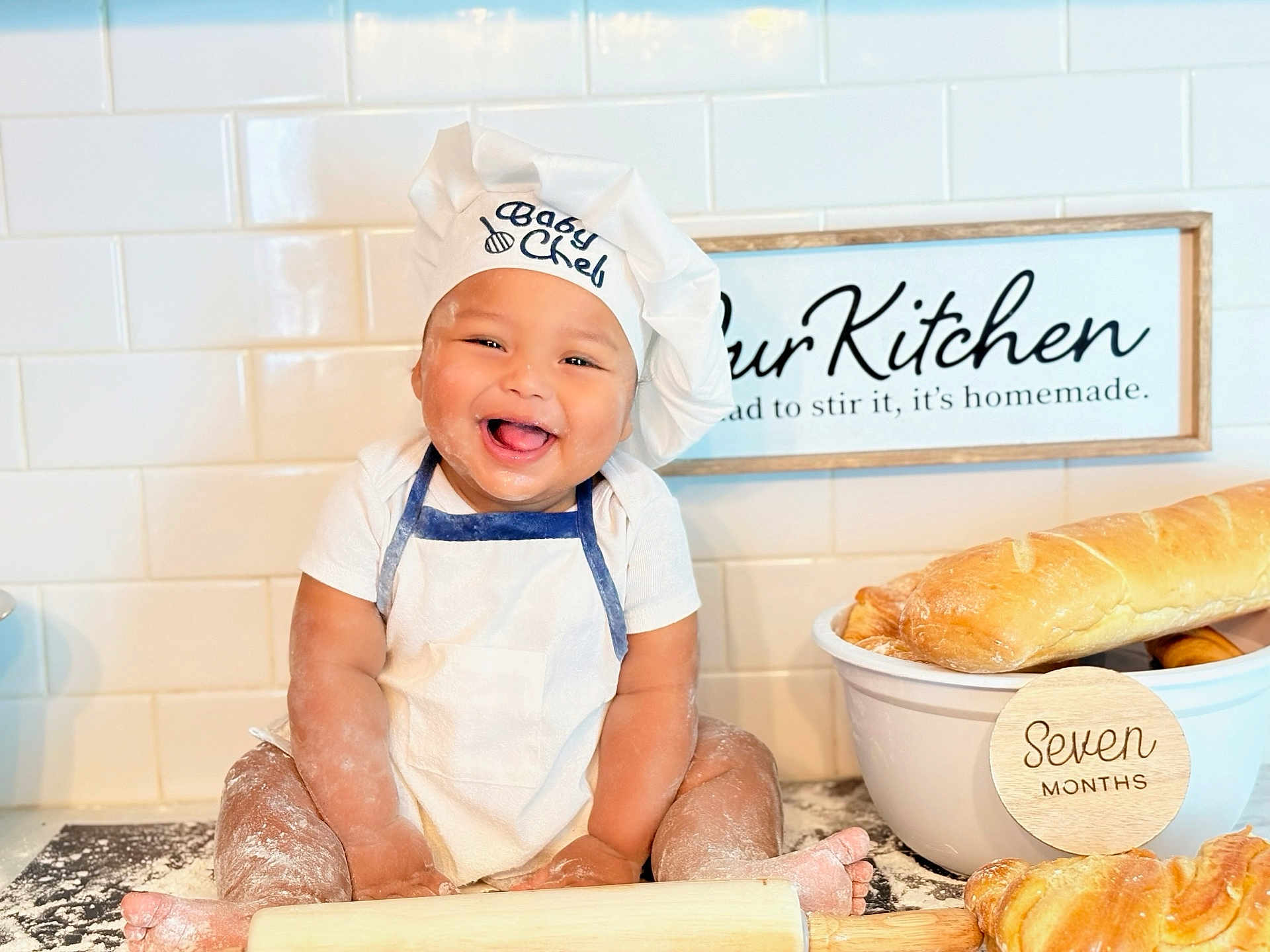 Ethan joined the competition — help win amazing prizes! baby, chef_hat, apron, flour, kitchen, baking, bread, croissant, rolling_pin, smiling, happy, infant, countertop, white_tiles, sign, cooking, cute, messy, child, portrait