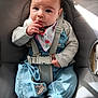 baby, infant, child, car_seat, seatbelt, overalls, bib, socks, hand, face, expression, indoor, light, clothing, person, cute, sitting, curious, soft, warm