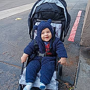 Eliel is registered to the contest to win money with this photo: asphalt, baby, blue_onesie, car, child, clothing, cute, daylight, footwear, happy, infant, outdoor, parking_lot, person, red_line, seat, smiling, stroller, toy_ears, transportation