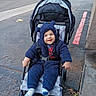 asphalt, baby, blue_onesie, car, child, clothing, cute, daylight, footwear, happy, infant, outdoor, parking_lot, person, red_line, seat, smiling, stroller, toy_ears, transportation
