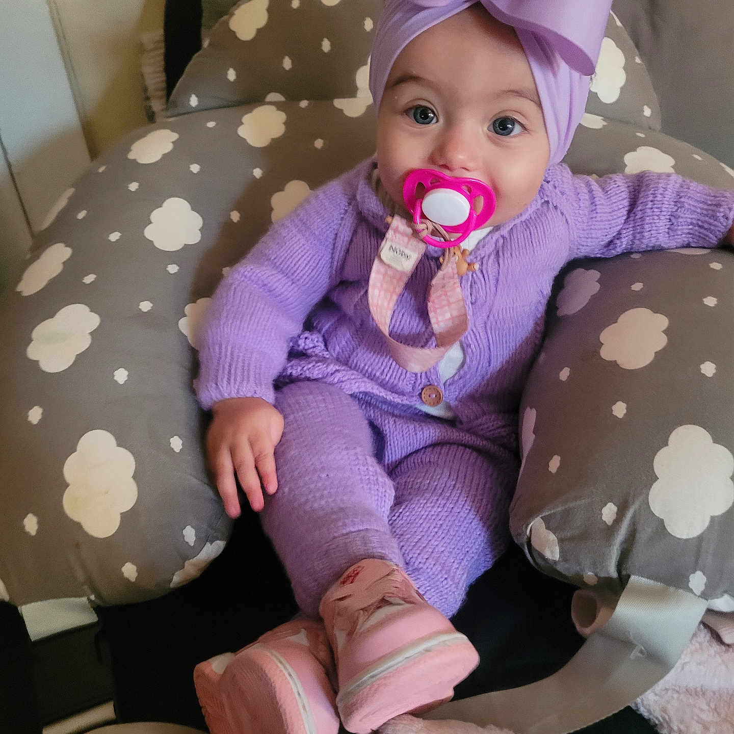 Suzanna is registered to the contest to win money with this photo: baby, baby_seat, blanket, bow, child, cloud_pattern, comfort, cozy, cute, headwrap, indoors, infant, knitwear, pacifier, pink_boots, portrait, purple_outfit, sitting, soft_toys, young_child