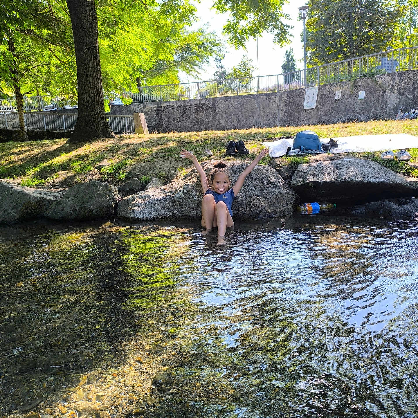 Eleena a rejoint le concours — aidez-le/la à gagner de superbes lots ! backpack, child, creek, daylight, grass, happy, nature, outdoor, park, play, river, rocks, shoes, smiling, summer, sunlight, towel, trees, water, water_reflection