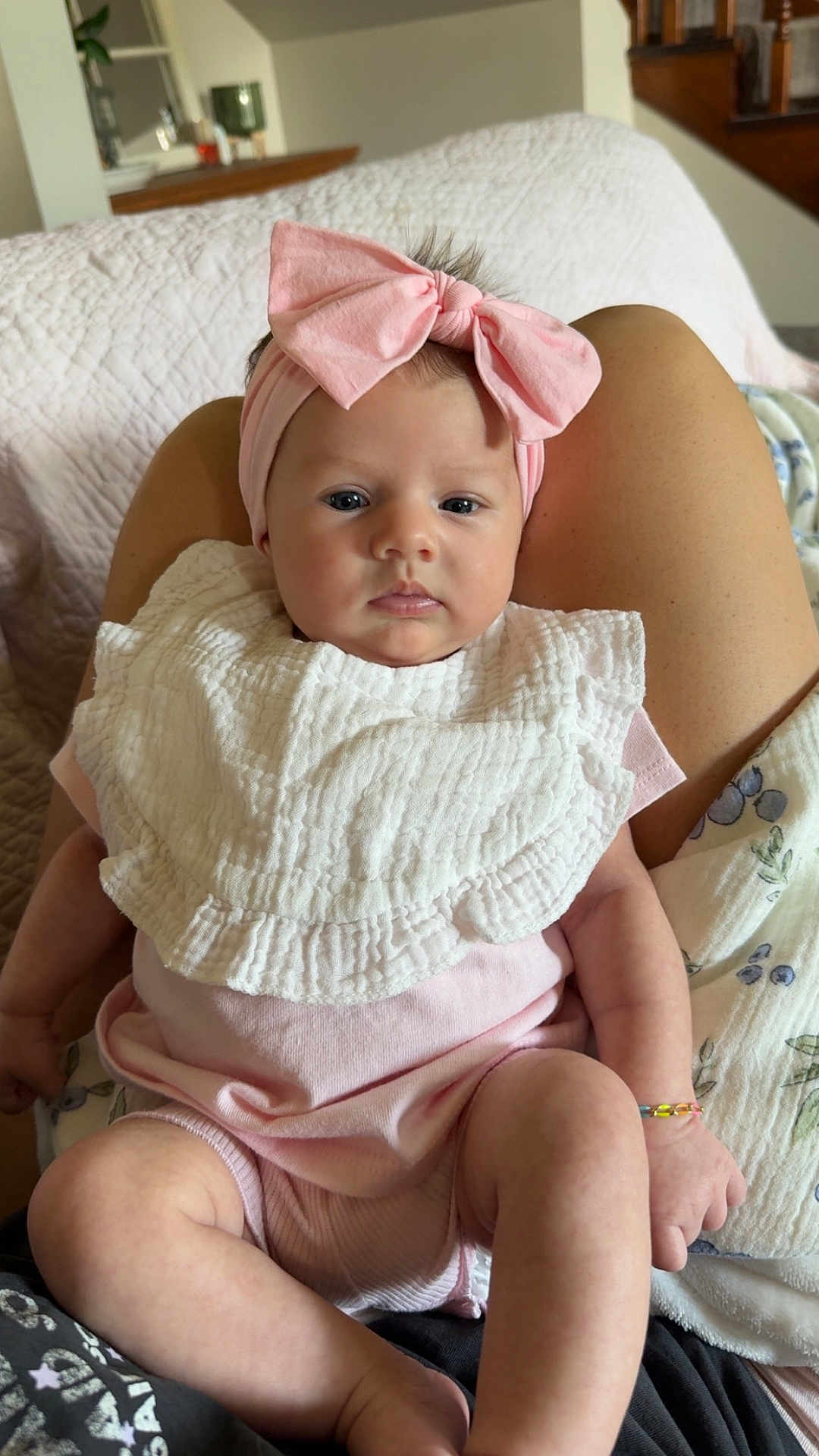 Hazel is registered to the contest to win money with this photo: baby, child, infant, pink_bow, headband, white_bib, pink_clothing, legs, hands, person, indoor, blanket, home, furniture, lap, skin, cute, portrait, sitting, curious