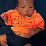 baby, infant, child, orange_clothing, black_shorts, bow, striped_bow, socks, lying_down, portrait, cute, dark_background, smiling, face, hands, feet, newborn, curly_hair, adorable, closeup