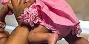 Brigette is registered to the contest to win money with this photo: baby, pink_outfit, arms, tattoos, indoor, legs, feet, hand, skin, infant, person, clothing, cute, child, holding, blurred_background, soft_light, playful, toddler, closeup