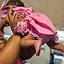 Brigette is registered to the contest to win money with this photo: baby, pink_outfit, arms, tattoos, indoor, legs, feet, hand, skin, infant, person, clothing, cute, child, holding, blurred_background, soft_light, playful, toddler, closeup