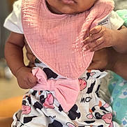 Brigette is registered to the contest to win money with this photo: baby, infant, child, pink_bib, cow_pattern, bow, clothing, hands, face, eyes, person, cute, closeup, soft_light, indoor, fabric, pattern, holding, skin, portrait