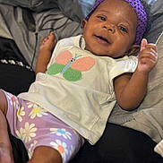 Brigette is registered to the contest to win money with this photo: baby, bed, blanket, butterfly_design, child, comfort, cute, flower_pattern, foot, hand, happy, indoors, infant, lying_down, person, purple_headband, purple_shorts, skin, smiling, white_shirt