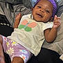 baby, bed, blanket, butterfly_design, child, comfort, cute, flower_pattern, foot, hand, happy, indoors, infant, lying_down, person, purple_headband, purple_shorts, skin, smiling, white_shirt