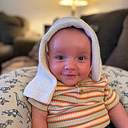 Jameson is registered to the contest to win money with this photo: baby, infant, smile, striped_shirt, hat, knit, dinosaur_pattern, pillow, indoor, lamp, cozy, cute, child, portrait, seated, denim, happy, face, eyes, warm_lighting