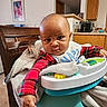 baby, baby_seat, bib, blanket, cabinet, carpet, child, curious, expression, face, furniture, home, indoor, infant, kitchen, person, plaid_clothing, table, toy, wooden_chair