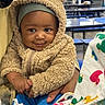Karter is registered to the contest to win money with this photo: baby, background_person, bench, cafeteria, child, colorful_cloth, cute, face, food_wrapper, fuzzy_clothing, hand, holding, indoor, infant, person, portrait, smile, table, teddy_bear_hoodie, warm_clothing