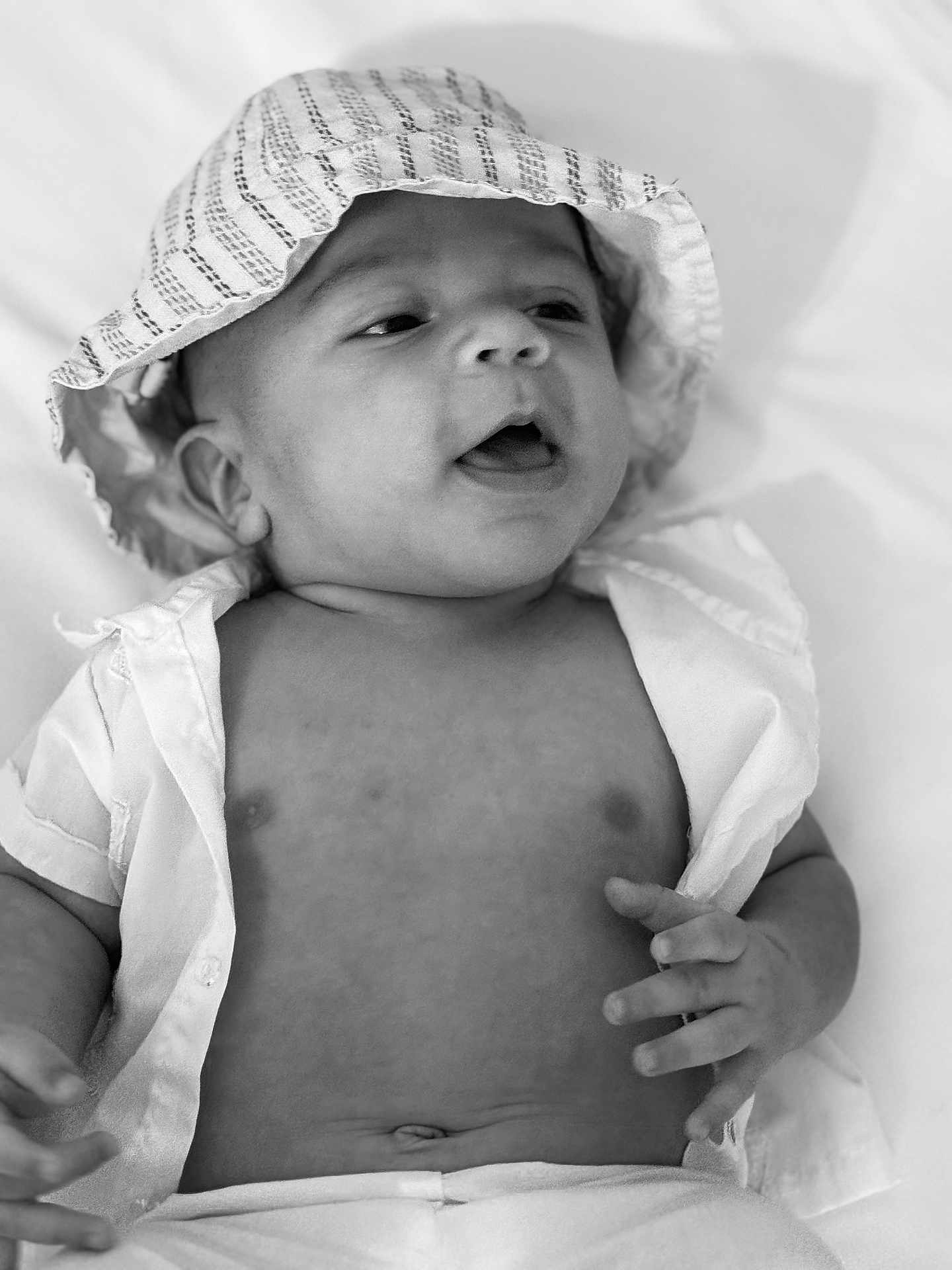 Mike is registered to the contest to win money with this photo: baby, infant, hat, striped_hat, shirt, open_shirt, lying_down, hand, mouth_open, black_and_white, portrait, cute, soft_light, skin, newborn, expression, child, young_child, closeup, face