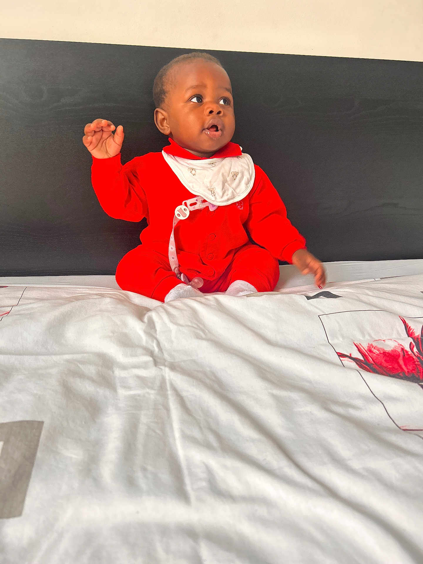 Alfredinho participe au concours pour gagner de l'argent avec cette photo : baby, child, red_onesie, bed, blanket, headboard, indoor, portrait, sitting, curious, infant, white_blanket, baby_bib, expression, face, looking_away, clothing, young_child, home, casual