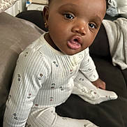 Dieu-Donné is registered to the contest to win money with this photo: baby, child, pajamas, sitting, indoors, face, curly_hair, earrings, couch, blanket, home, cozy, cute, expression, infant, person, clothing, comfortable, portrait, furniture