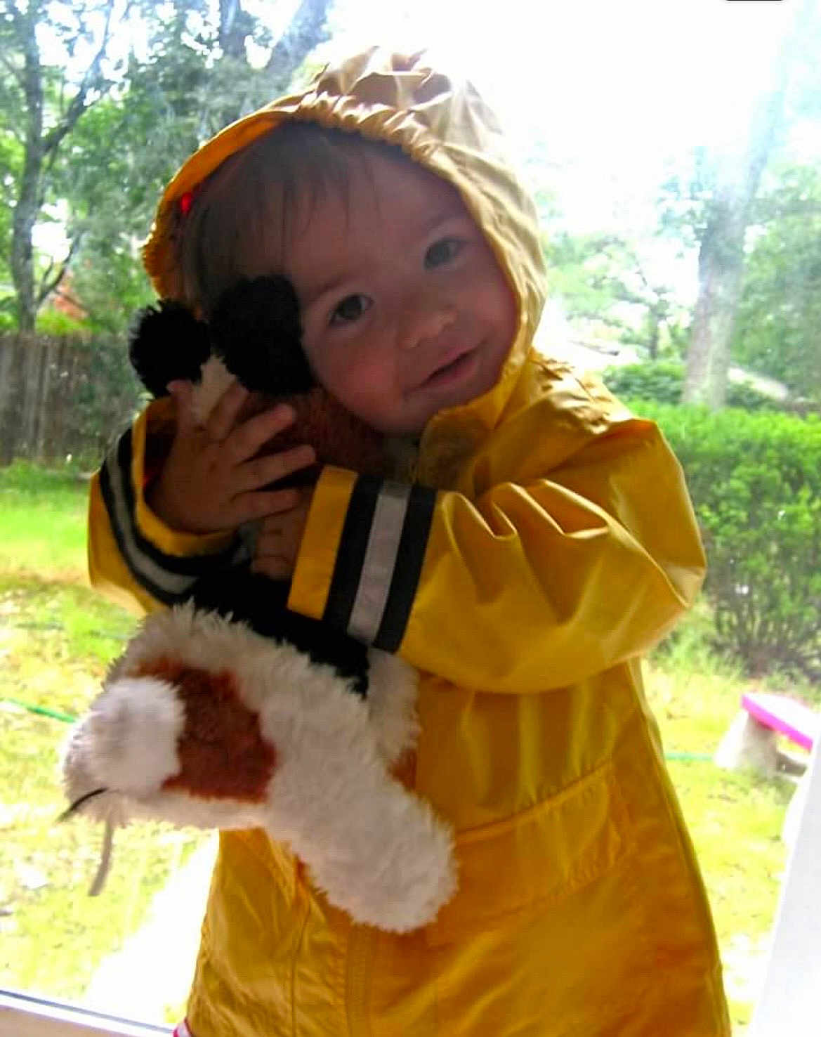 Samuel is registered to the contest to win money with this photo: toddler, child, yellow_raincoat, stuffed_animal, hugging, indoor, window, outdoor, greenery, raincoat_hood, plush_toy, cute, portrait, smiling, young_child, playing, cozy, childhood, happy, soft_light