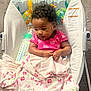 baby, infant, child, pink_shirt, blanket, baby_bottle, baby_rocker, animal_print, curly_hair, indoor, carpet, cute, child_seat, floral_pattern, toddler, baby_toys, baby_care, smiling, playful, resting