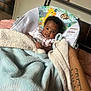 baby, blanket, baby_seat, animal_print, giraffe, sloth, hand, tattoo, pacifier, bedroom, furniture, person, infant, smile, curly_hair, comfort, indoor, cozy, child, cute