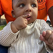 Saif joined the competition — help win amazing prizes! baby, child, person, face, hand, finger, clothing, onesie, orange_shirt, outdoor, grass, fence, car, seated, curious, closeup, portrait, expression, skin, casual