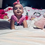 Luciana is registered to the contest to win money with this photo: baby, pink_headband, pink_shirt, stuffed_animals, bed, blanket, floral_pattern, teddy_bear, child, cute, smiling, indoors, portrait, infant, toy, cozy, happy, lying_down, headband, soft_toys