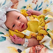 Lilith joined the competition — help win amazing prizes! baby, newborn, infant, yellow_clothing, headband, bow, hospital_bracelet, blanket, floral_pattern, sunflower, soft_lighting, portrait, cute, child, lying_down, closeup, face, skin, hand, sleepwear