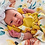 baby, newborn, infant, yellow_clothing, headband, bow, hospital_bracelet, blanket, floral_pattern, sunflower, soft_lighting, portrait, cute, child, lying_down, closeup, face, skin, hand, sleepwear
