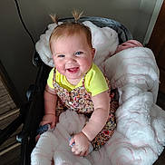 Preszley is registered to the contest to win money with this photo: baby, blanket, blue_eyes, child, clothing, cozy, cute, door, floral_dress, happy, indoor, infant, person, pigtails, smile, soft_texture, stroller, wall, wood_floor, yellow_shirt