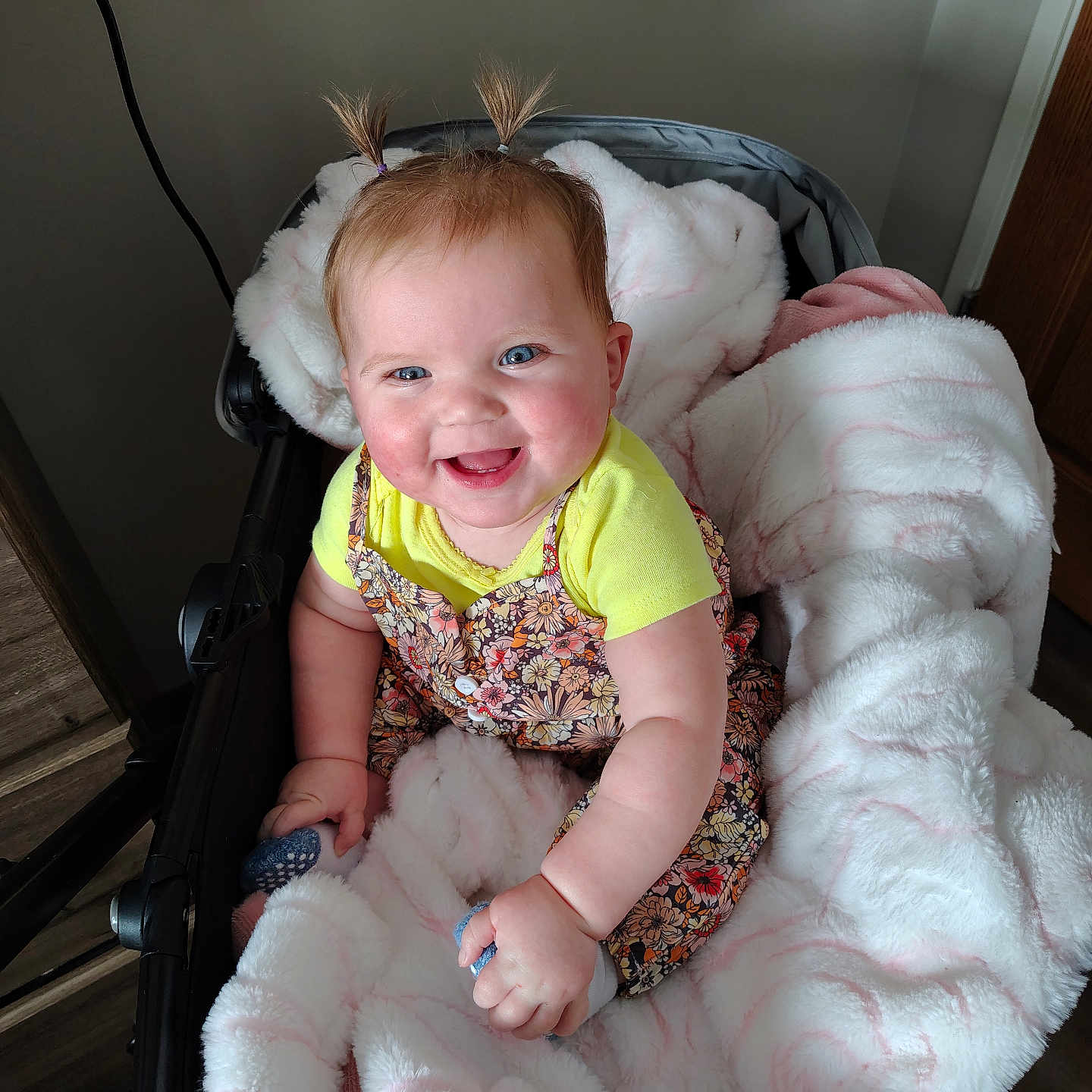 Preszley is registered to the contest to win money with this photo: baby, blanket, blue_eyes, child, clothing, cozy, cute, door, floral_dress, happy, indoor, infant, person, pigtails, smile, soft_texture, stroller, wall, wood_floor, yellow_shirt
