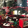 cat, christmas_tree, ornaments, plush_toy, gingerbread, snowman, tree_skirt, red, green, decorations, holiday, indoor, carpet, vintage_tv, festive, curious, pet, relaxed, home, seasonal