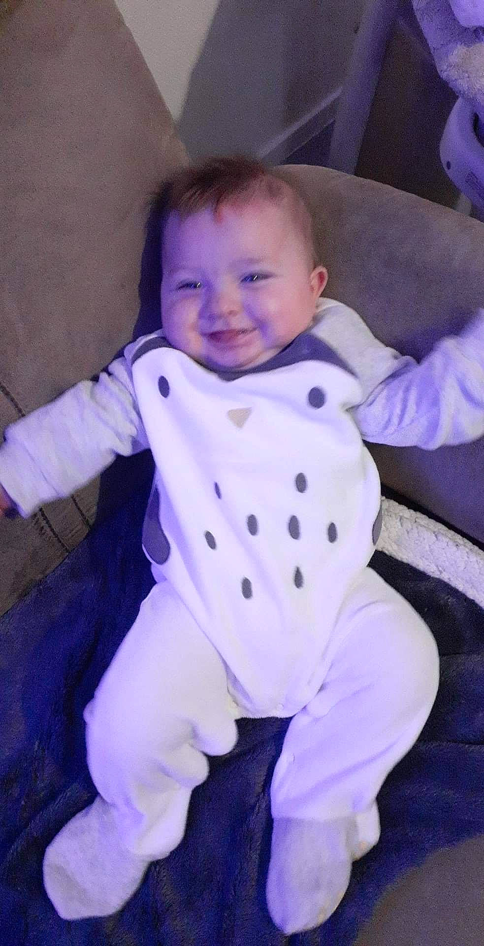 Haïden participe au concours pour gagner de l'argent avec cette photo : baby, baby_products, baby_toddler_clothing, barefoot, chair, child, comfort, electric_blue, eye, face, flooring, happy, infant_bodysuit, joy, pattern, person, purple, sitting, sleeve, smile