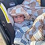baby, blanket, car_seat, child, cozy, checkered_pattern, outdoor, sunlight, face, wide_eyes, clothing, infant, warm, cute, comfort, person, portrait, seat, fabric, baby_gear